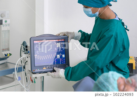 Multi-parameter patient monitor in operating room, controlled by nurse in surgical green gown uniform. 102224093