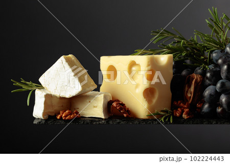Cheese with walnuts, blue grapes, and rosemary on a black background. Cheese with walnuts, blue grapes, and rosemary on a black background. 102224443