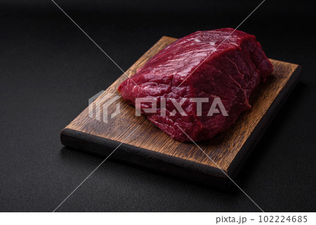 A piece of fresh raw beef with salt, spices and herbs on a wooden cutting board A piece of fresh raw beef with salt, spices and herbs on a wooden cutting board 102224685