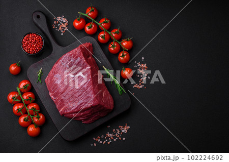 A piece of fresh raw beef with salt, spices and herbs on a wooden cutting board A piece of fresh raw beef with salt, spices and herbs on a wooden cutting board 102224692
