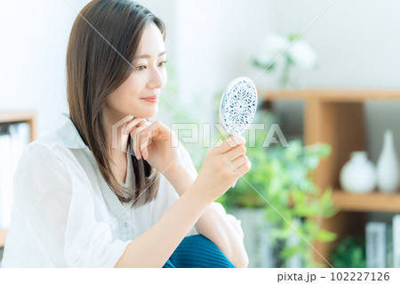 リビングで手鏡を見ながらスキンケアをする若い女性 102227126