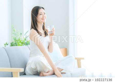 リビングでソファに座って水を飲む若い女性 102227136