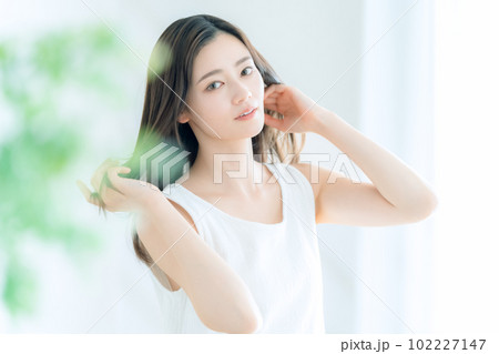 リビングの窓際でヘアケアをする若い女性 102227147