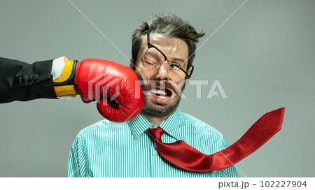 Mature man, businessman in red tie getting boxing punch in jaw from business competitors over grey background. Concept financial loses, business fall, deadlines, economic crisis 102227904