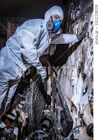 a specialist in a protective suit from a cleaning company cleans a destroyed housing after a fire a specialist in a protective suit from a cleaning company cleans a destroyed housing after a fire 102229039