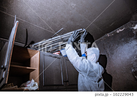 a specialist in a protective suit from a cleaning company cleans a destroyed housing after a fire a specialist in a protective suit from a cleaning company cleans a destroyed housing after a fire 102229043