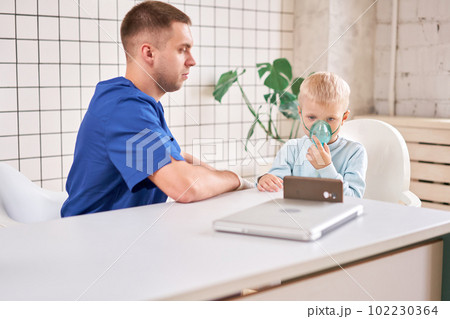 A pediatrician diagnoses lung disease and provides treatment. Breathe the medicine through a nebulizer inhaler.. Portrait of adorable little boy visiting doctor. A pediatrician diagnoses lung disease and provides treatment. Breathe the medicine through a nebulizer inhaler.. Portrait of adorable little boy visiting doctor. 102230364