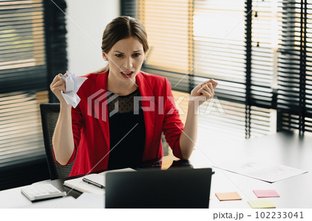 Furious caucasian businesswoman sitting at desk and crumpling paper, having problem with project Furious caucasian businesswoman sitting at desk and crumpling paper, having problem with project 102233041