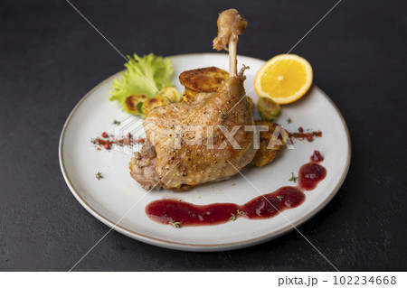 Duck leg confit with Brussels sprouts, baked potatoes, thyme, orange and lingonberry sauce. Traditional French cuisine. Selective focus, close-up, black background. Duck leg confit with Brussels sprouts, baked potatoes, thyme, orange and lingonberry sauce. Traditional French cuisine. Selective focus, close-up, black background. 102234668
