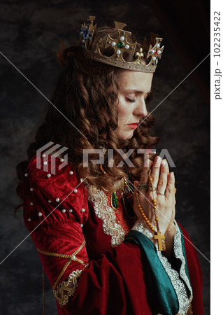 medieval queen in red dress with rosary and crown praying 102235422