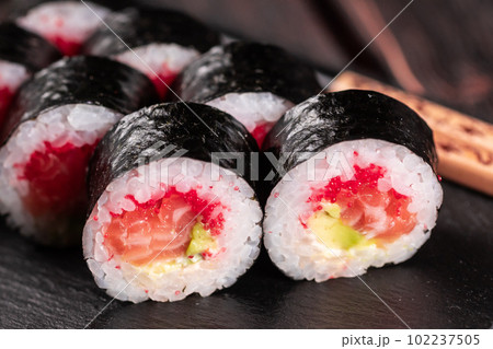 Maki sushi roll with salmon avocado and tobiko caviar served on black board close-up - Japanese food 102237505