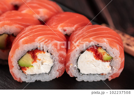 Sushi roll maguro with salmon avocado and tobiko, philadelphia cheese on black board close-up. Sushi menu. Japanese food. Sushi roll maguro with salmon avocado and tobiko, philadelphia cheese on black board close-up. Sushi menu. Japanese food. 102237508