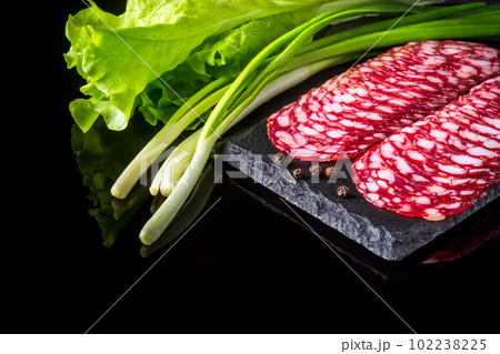 Sliced salami on a slate serving Board and salad greens with onion. Black isolated background 102238225