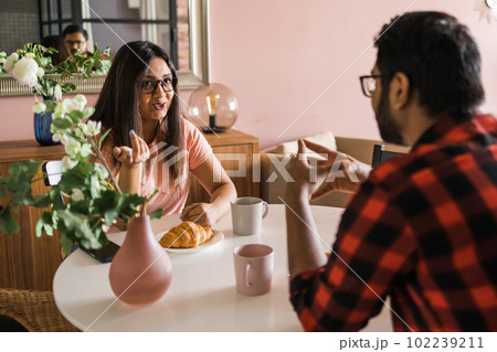 Happy couple eating breakfast and talking at dining table in morning. Indian girl and latino guy. Relationship and diversity concept 102239211