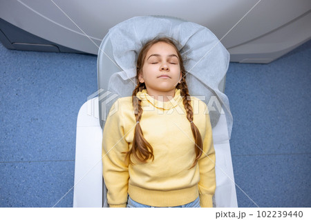 Little girl keeps eyes closed moving into mri scan machine before undergoing medical examination. Little girl keeps eyes closed moving into mri scan machine before undergoing medical examination. 102239440
