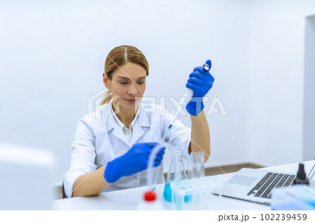Female scientist in protective gloves dropping liquid substance into the test tube with a pipette 102239459