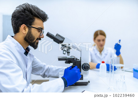 Health care researchers working in science laboratory, microscoping, looking focused at microscope 102239460