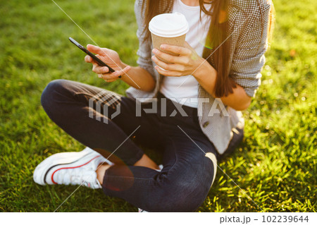 The girl holds the phone and coffee in hand. Sunset. Summertime. 102239644