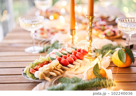 Christmas dinner feast. A small table is served with snacks, bruschettas, and canapes. A decorated dining table with champagne glasses, candles and christmas tree an garland in background 102240036