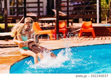 Dad and daughter have fun and and sit on the edge of the pool  102240037