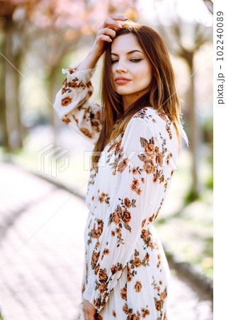 Beautiful young woman near the blooming spring tree. Attractive girl enjoying her time outside in park. 102240089