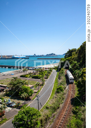黄金の朝焼けの宮崎県日南市油津港岩場の波打ち際を輝きながら走る通勤列車の日南線キハ40 102240759