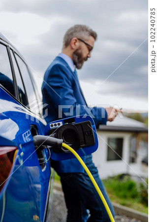 Mature businessman waiting for charging his electric car. Mature businessman waiting for charging his electric car. 102240785