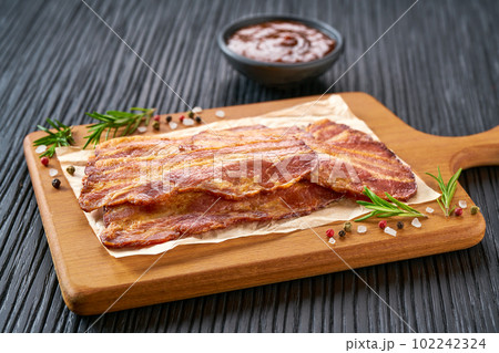 fried bacon strips and bbq sauce on a black table, selective focus. fried bacon strips and bbq sauce on a black table, selective focus. 102242324