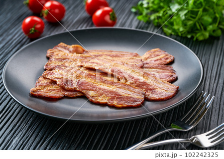 plate with fried bacon and bbq sauce on a black table.  Plate with fried bacon on black  kitchen table. 102242325