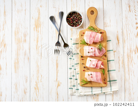 Rolls of smoked bacon and rosemary on a white table, top view. Rolls of smoked bacon and rosemary on a white table, top view. 102242411
