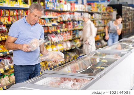 Aged man choosing frozen chicken in glass refrigerator in supermarket 102244082