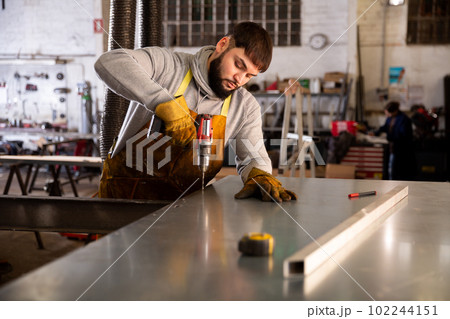 Man engineer drilling metal sheet in workshop 102244151
