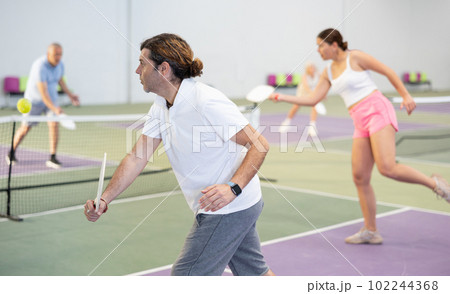 Athletic man and partner playing pickleball tennis on the pickleball court indoors 102244368
