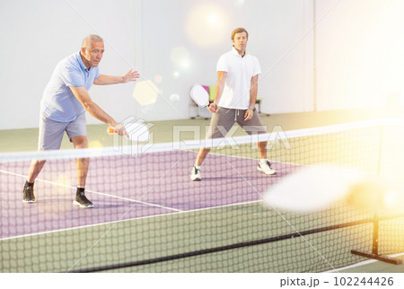 Aged man playing doubles pickleball match with male partner Aged man playing doubles pickleball match with male partner 102244426