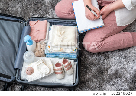 Top view of pregnant woman writing packing list for maternity hospital sitting next to suitcase 102249027
