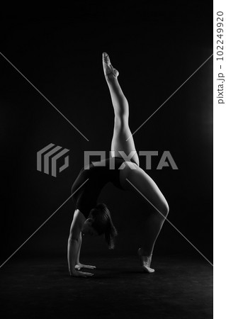 Flexible girl, rhythmic gymnastics artist jumping on white dark background. Grace in motion, action. 102249920