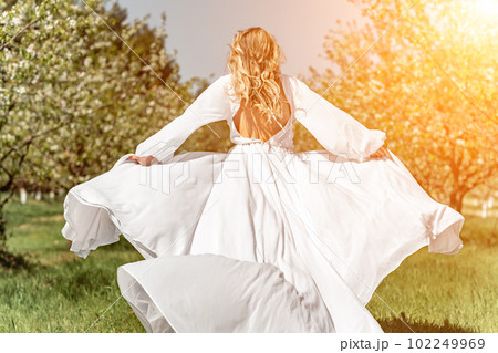 Woman white dress park. A woman in a white dress runs through a blossoming cherry orchard. The long dress flies to the sides, the bride runs rejoicing in life. 102249969
