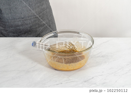 Mixing wet ingredients in a large glass mixing bowl to bake white chocolate macadamia nut. Mixing wet ingredients in a large glass mixing bowl to bake white chocolate macadamia nut. 102250112