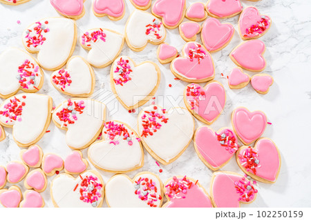 Decorating heart-shaped sugar cookies with pink and white royal icing for Valentine's Day. 102250159