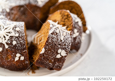 Sliced gingerbread bundt cake with caramel filling, buttercream frosting, and powdered sugar dusting on the cake plate. 102250172