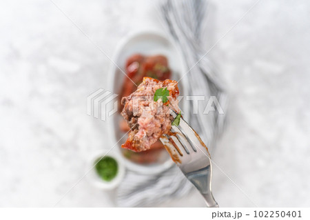 Flat lay. Slicing classic meatloaf with a sweet glaze on a white serving plate 102250401