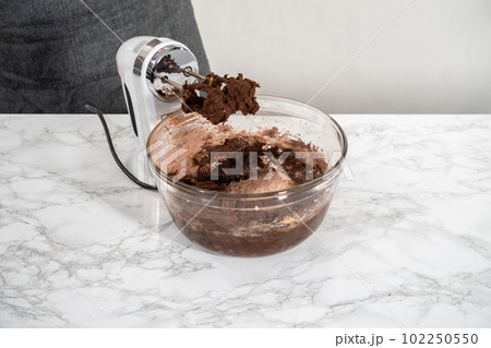 Mixing ingredients in a large glass mixing bowl to bake peppermint white chocolate cookies. 102250550