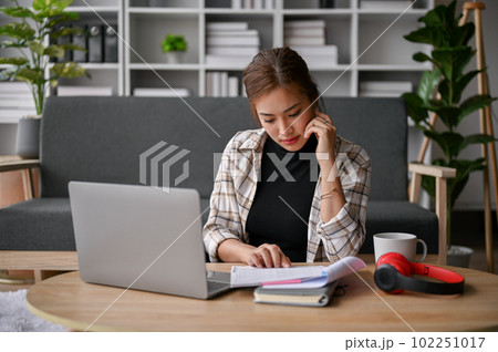 Focused young Asian female freelancer reading documents in her living room. Focused young Asian female freelancer reading documents in her living room. 102251017