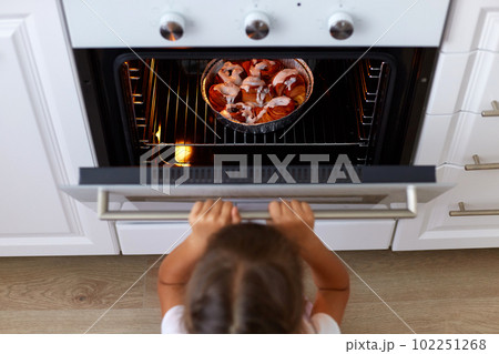 Top view of girl child opening oven looking at tasty croissant or other baking n the oven, cooking process on kitchen, small dark haired female kid wants delicious sweets. Top view of girl child opening oven looking at tasty croissant or other baking n the oven, cooking process on kitchen, small dark haired female kid wants delicious sweets. 102251268