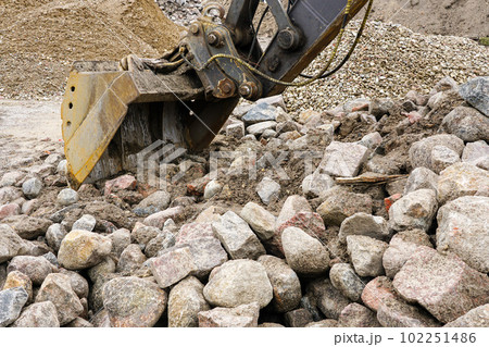 The bucket of a large hydraulic excavator rakes rocks into a pile 102251486