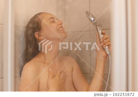 Indoor shot of beautiful young adult woman with naked body taking shower, standing under water with satisfied facial expression, enjoying relaxation in bathroom. Indoor shot of beautiful young adult woman with naked body taking shower, standing under water with satisfied facial expression, enjoying relaxation in bathroom. 102251672