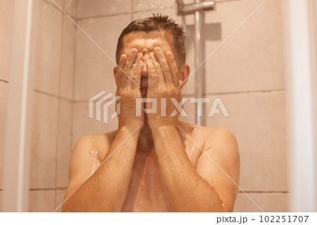 Indoor shot of young adult handsome dark haired man taking shower, covering face with palm, washing his body, everyday hygiene routine and refreshment. Indoor shot of young adult handsome dark haired man taking shower, covering face with palm, washing his body, everyday hygiene routine and refreshment. 102251707