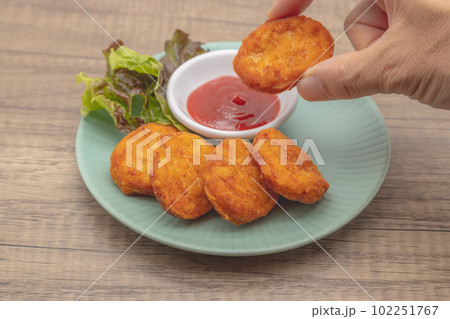 チキンナゲットとケチャップが青い皿に盛り付けられている　右手でナゲットをもってケチャップを付けている 102251767