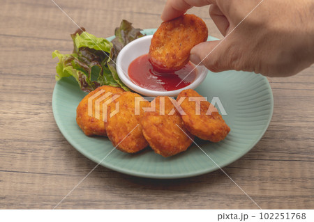 チキンナゲットとケチャップが青い皿に盛り付けられている　ナゲットを手に持ってケチャップに付けている 102251768
