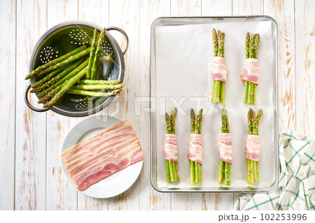 bundle of green beans wrapped in bacon on baking tray, preparation for baking, top view. 102253996